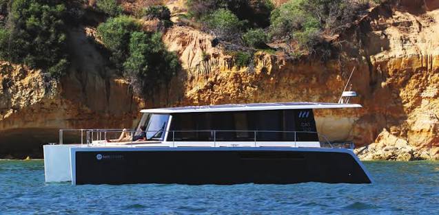 The catamaran in profile along the Costa Brava cliffs